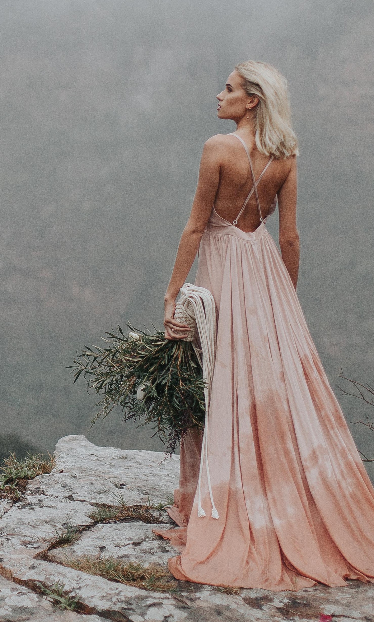 Oh Happy Day striking boho bride with blush dress and exposed back holding natural greenery bouquet